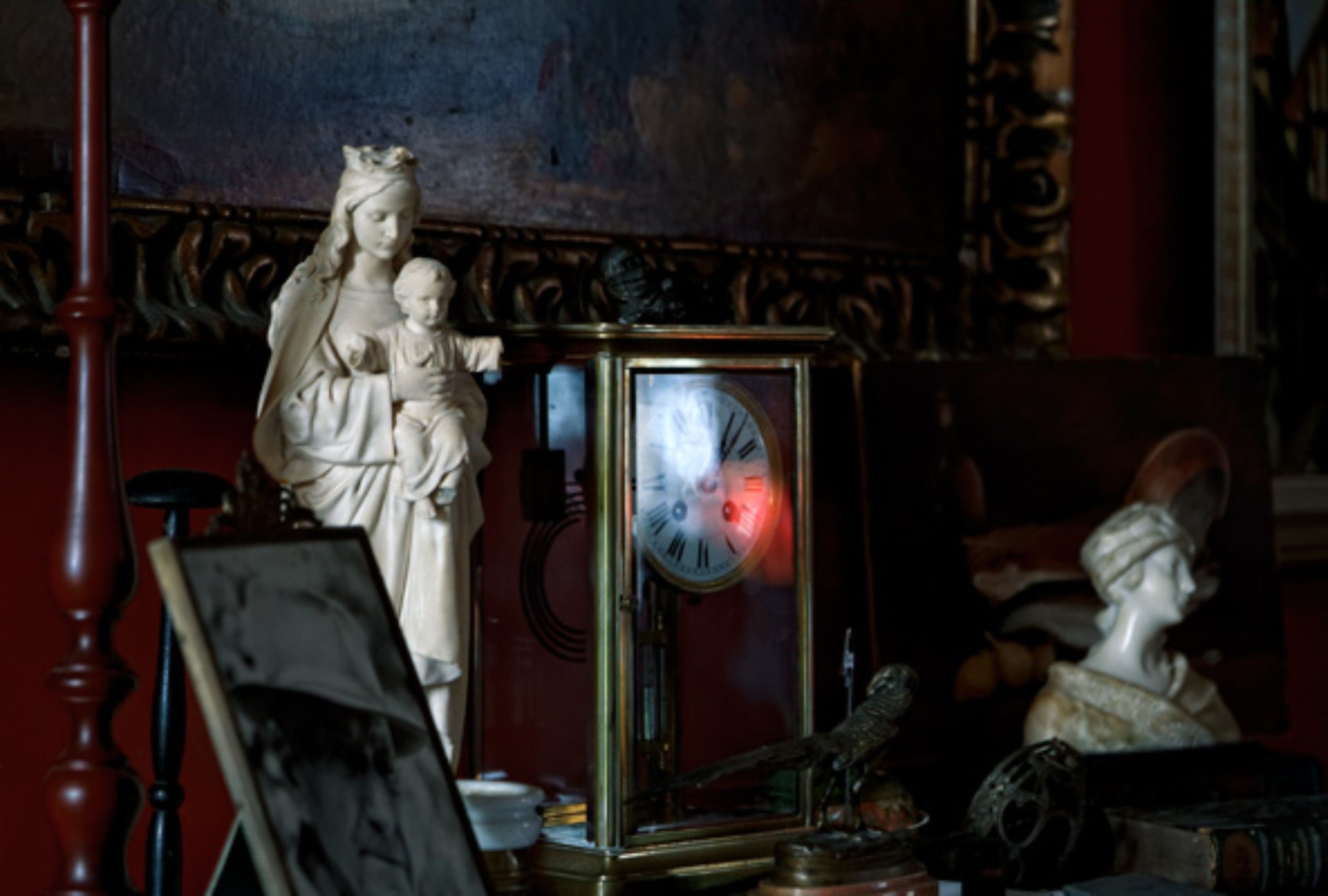 A statue of a woman holding a child, a clock, and a bust in a room with ornate woodwork.