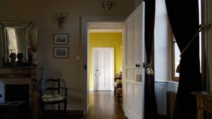A hallway with wooden flooring leading to a white door. There is a chair and a fireplace on the left side.