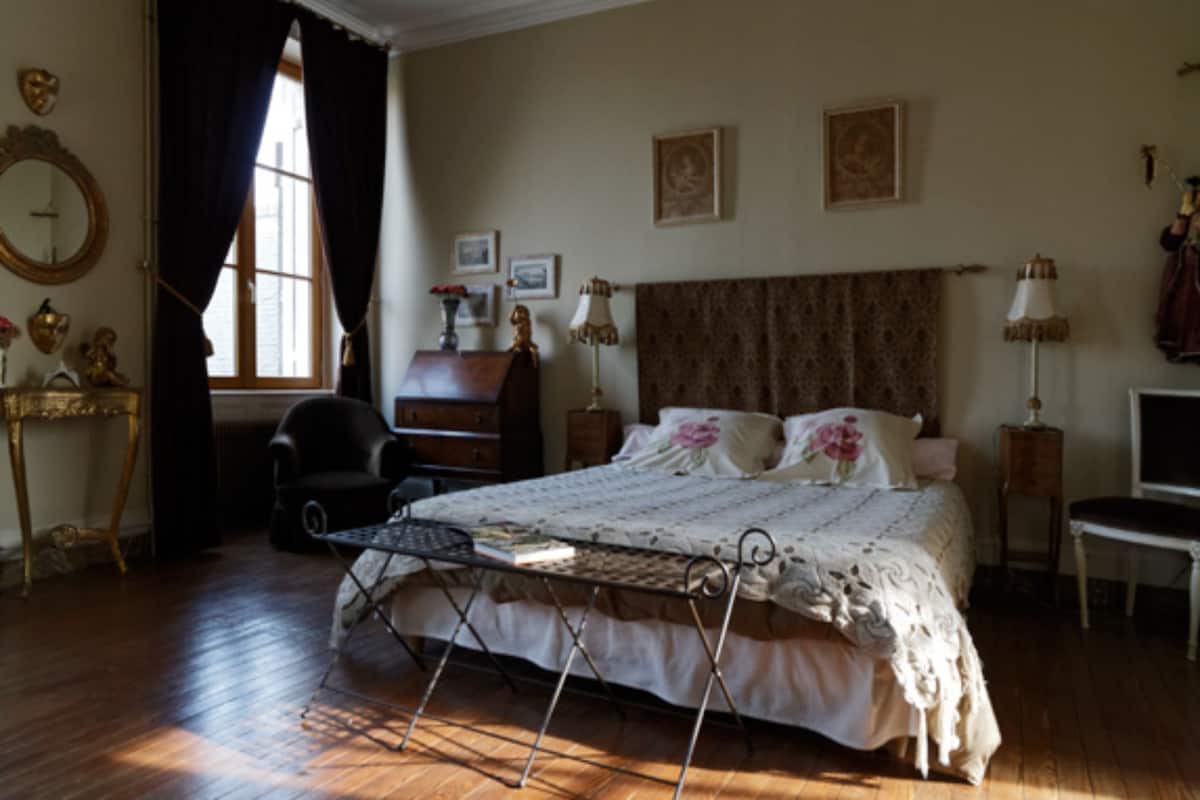 A bedroom with a bed, a desk, a chair, a lamp, and a window with curtains.