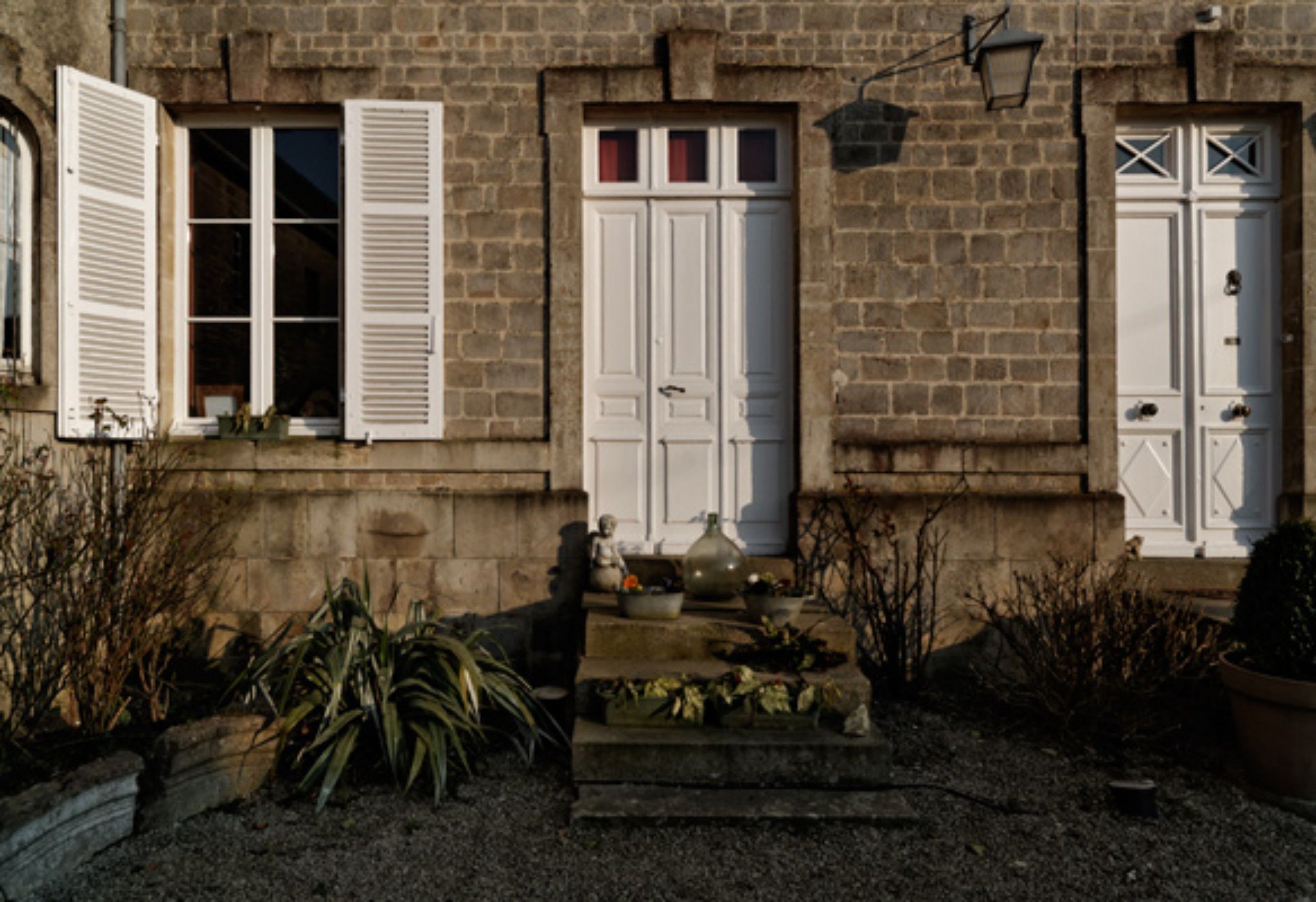 A stone building with white doors and shutters, a small porch with steps, and potted plants.