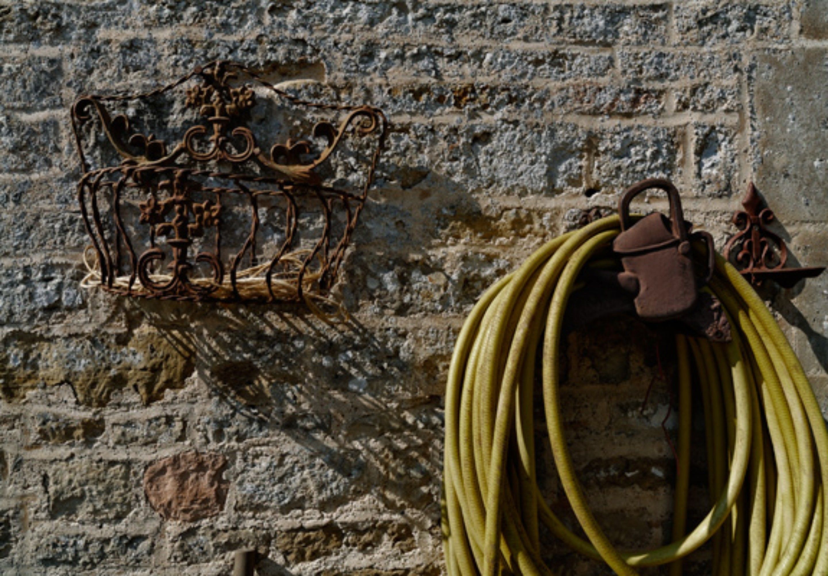 A metal structure with a crown-like design against a stone wall, and a coiled hose hanging nearby.