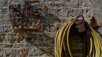 A metal structure with a crown-like design against a stone wall, and a coiled hose hanging nearby.