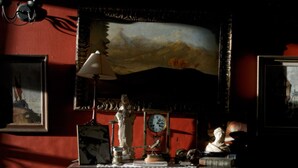 A room with a clock, a statue, and a painting on the wall.