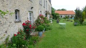 A stone building with a garden, a lawn, and a table with chairs.