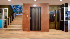 A hotel lobby with a marble staircase, a closed elevator, and a mural on the wall. - OYO 19910 Hotel Sapphire Paradise (Ooty)