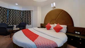 A hotel room with a large bed, a headboard, a nightstand, a desk, and a patterned wall. - OYO 19910 Hotel Sapphire Paradise (Ooty)