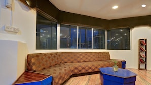 A corner living room with a brown patterned sofa, two blue side tables, and a bookshelf. - OYO 19910 Hotel Sapphire Paradise (Ooty)