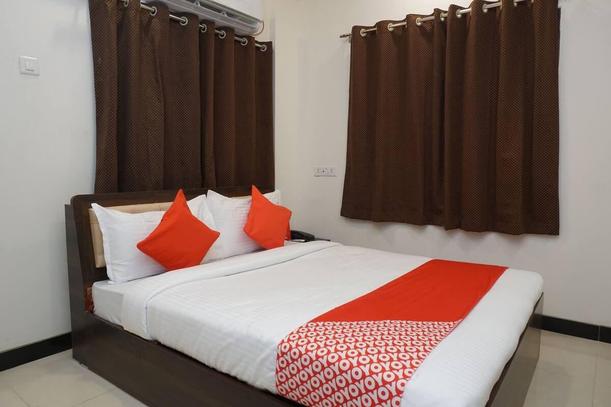 A neatly made bed with white bedding and orange accents, a brown headboard, and a patterned throw.