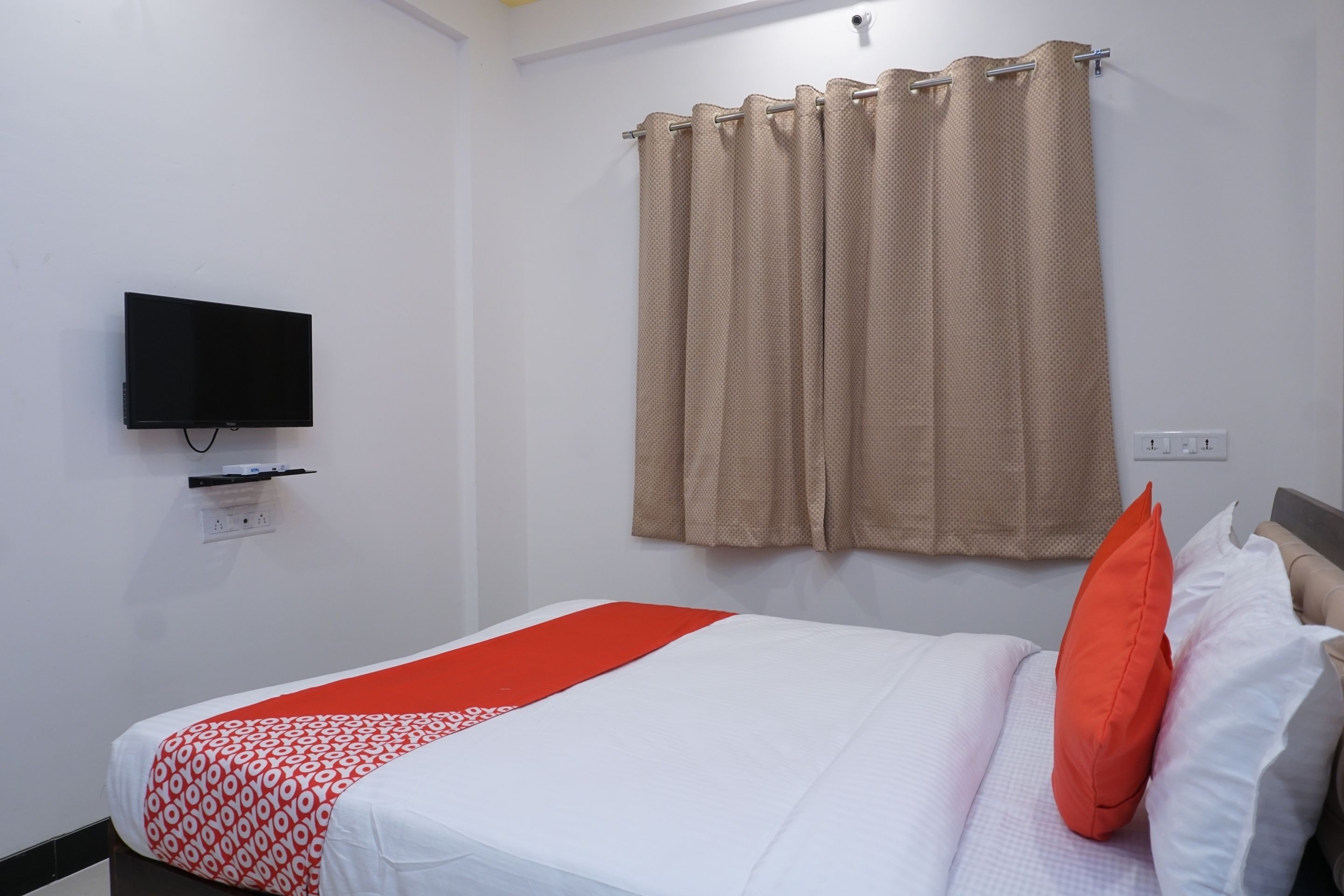 A hotel room with a bed, a television mounted on the wall, and a window with curtains.