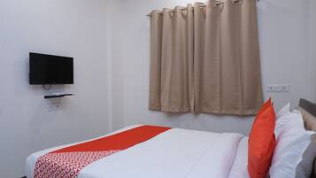 A hotel room with a bed, a television mounted on the wall, and a window with curtains.