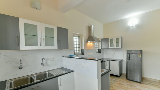 A modern kitchen with white and grey cabinetry, a stainless steel sink, and a built-in oven. - OYO 18602 Home Spacious Stay Near Lulu Mall (Kanayannur)