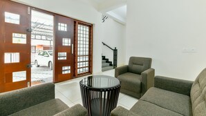 A living room with a glass-top coffee table, two grey sofas, and a wooden door leading outside. - OYO 18602 Home Spacious Stay Near Lulu Mall (Kanayannur)