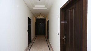 A hallway with a dark wooden door on the right, a light-colored tiled floor, and a ceiling with recessed lighting. - OYO 19334 Flagship Shanta Inn Charbagh (Lucknow)