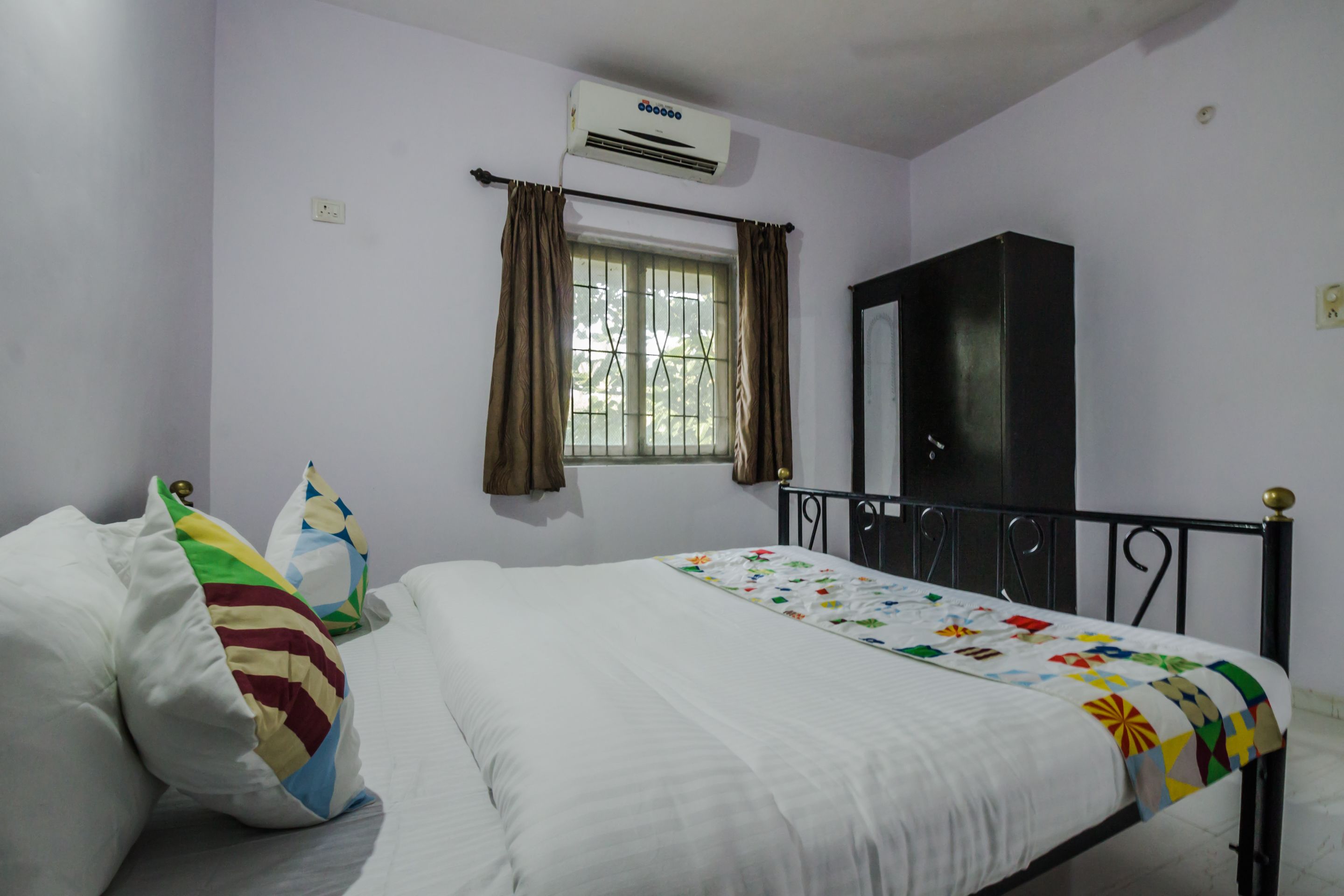 A bedroom with a bed, a wardrobe, an air conditioning unit, and a window with curtains.