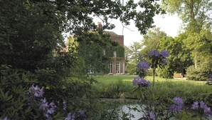 A garden with a pond, purple flowers, and a brick building in the background. - Mulberry House (Ongar)