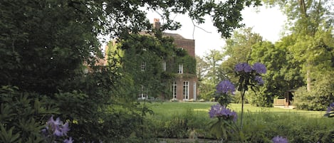 A garden with a pond, purple flowers, and a brick building in the background.
