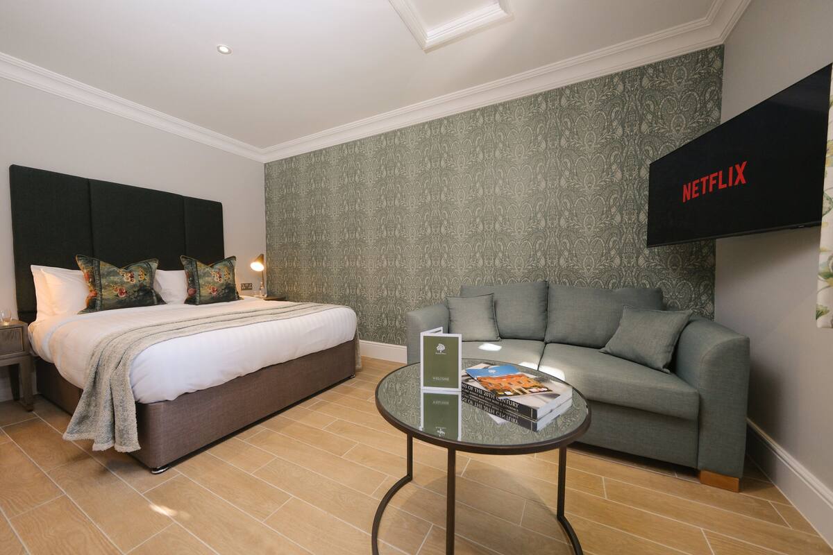 A hotel room with a bed, a sofa, a coffee table with a book, and a TV mounted on the wall.