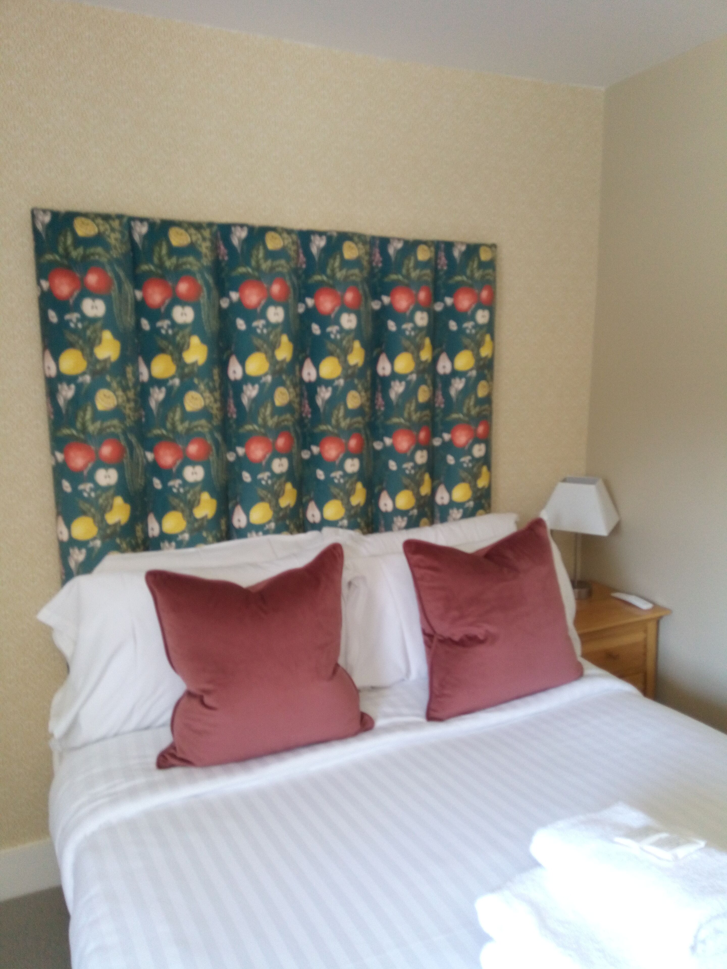 Una camera d'albergo con un letto, due cuscini, un comodino, una lampada e una parete decorata con un motivo a frutta.
