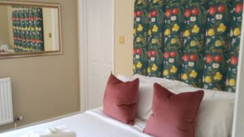 A neatly made bed with white linens and two red pillows, a white door, and a wall with a patterned tapestry.