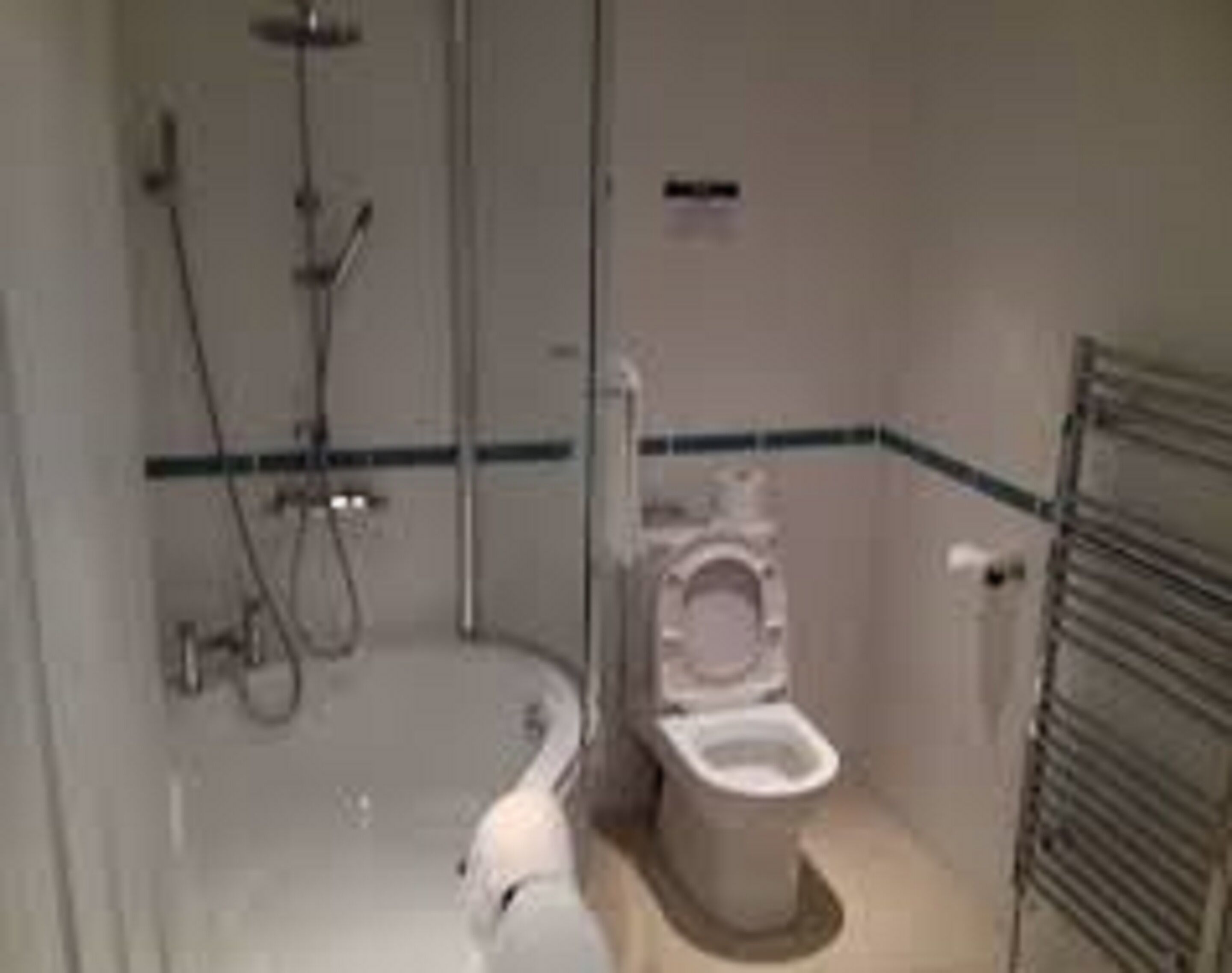A small, compact bathroom with a toilet, a shower, and a towel rack.