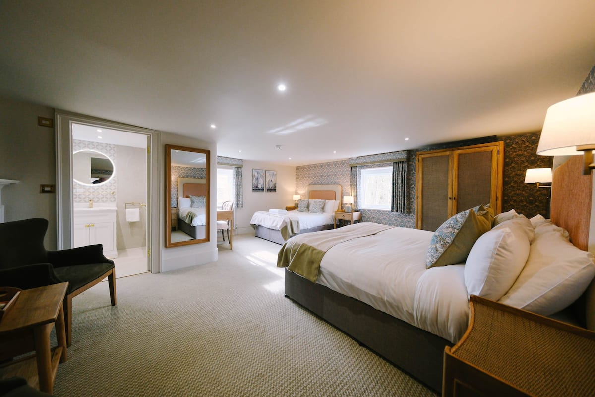A hotel room with a large bed, a desk, a chair, a mirror, and a bathroom visible through an open door.