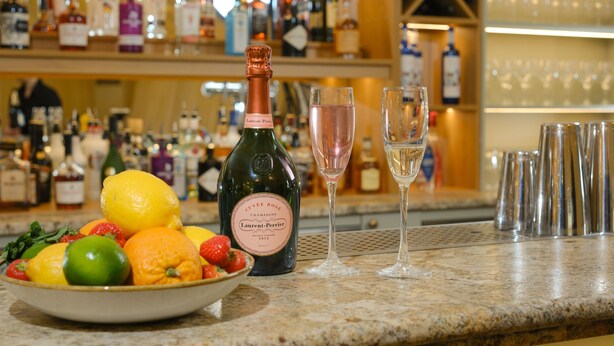 A bar counter with a bottle of champagne, two glasses, and a bowl of fruit. - Mulberry House (Ongar)