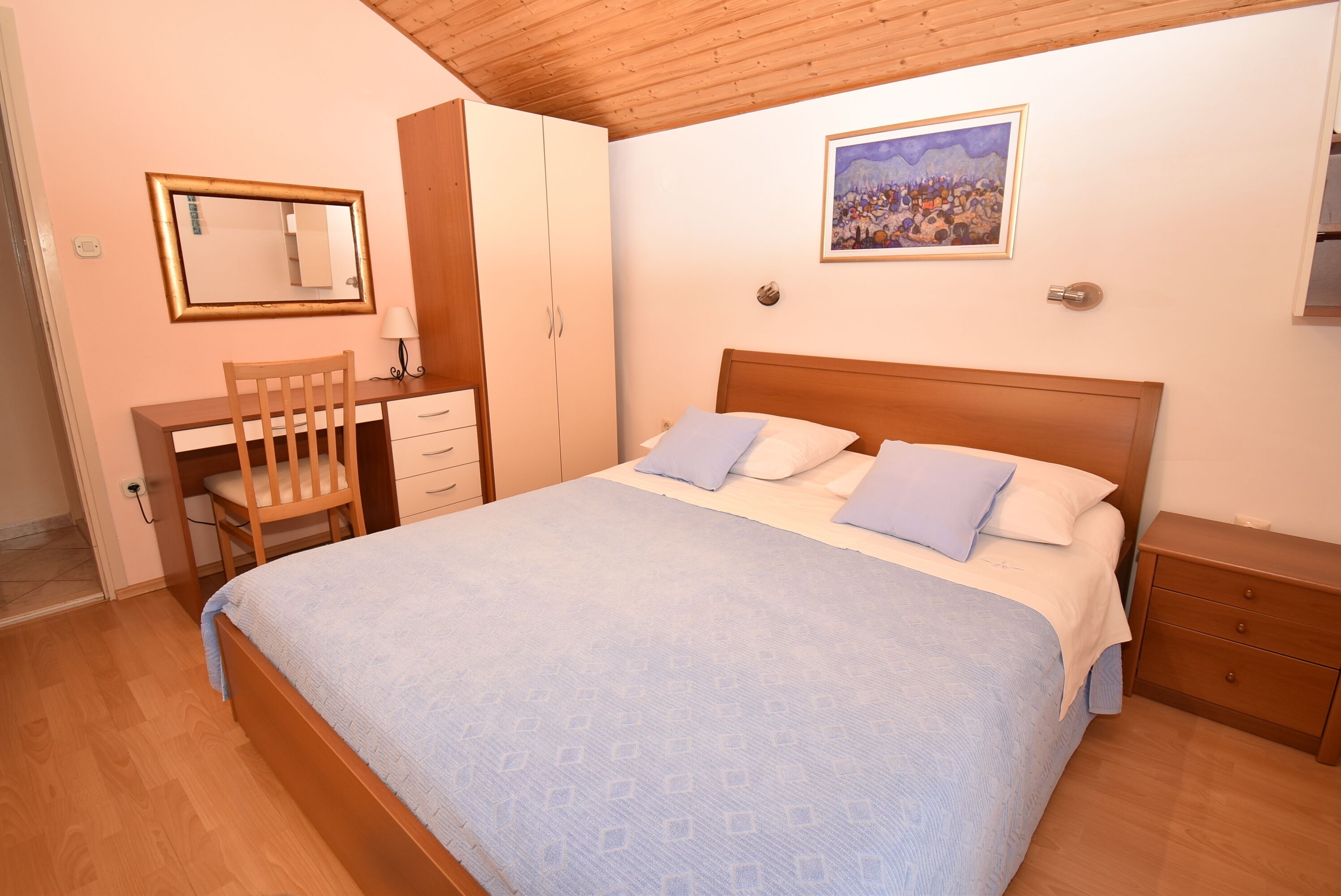 A bedroom with a bed, a desk, a chair, a wardrobe, and a painting on the wall.