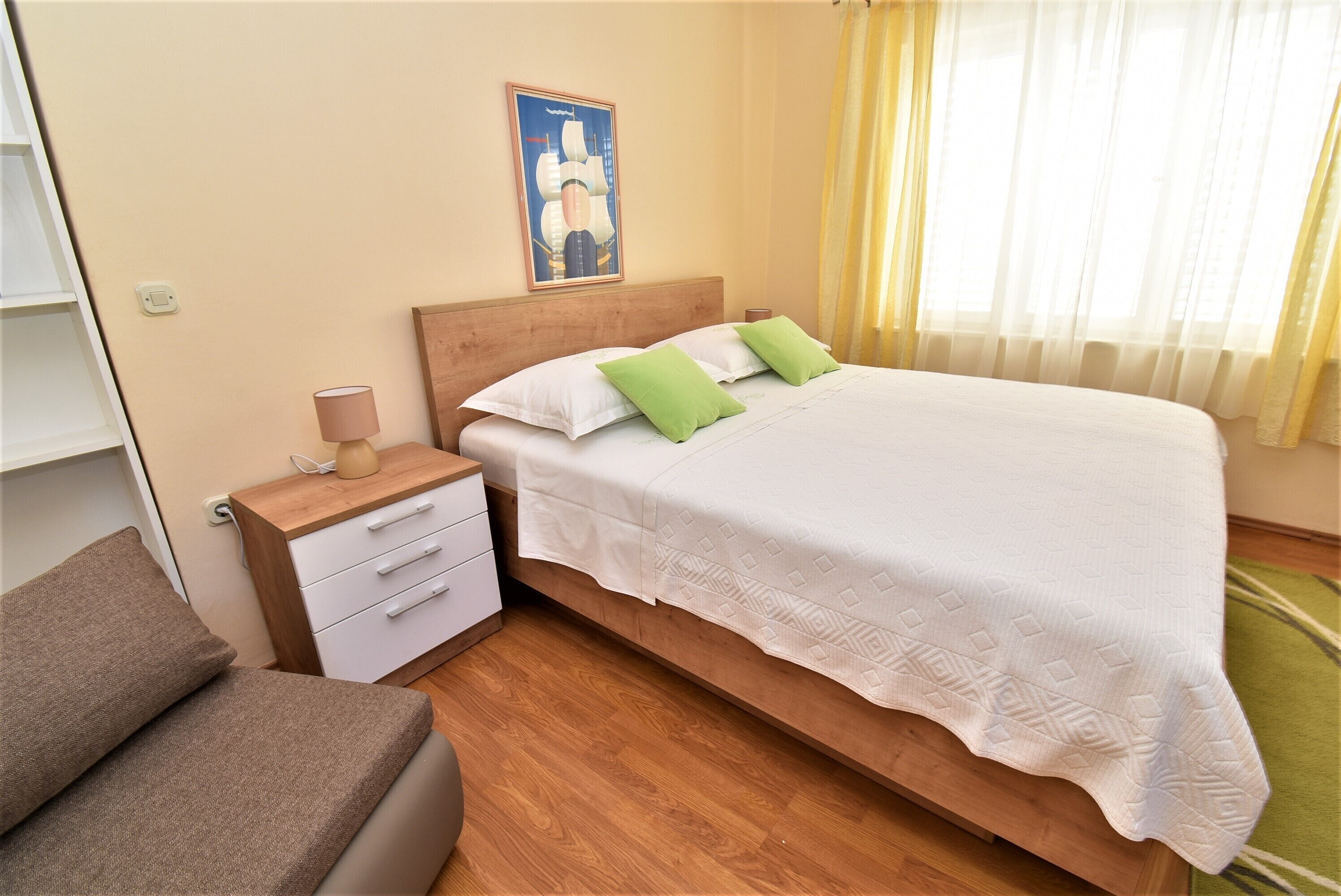 Un dormitorio ordenado con una cama de madera, ropa de cama blanca, una mesita de noche con una lámpara y una almohada verde.