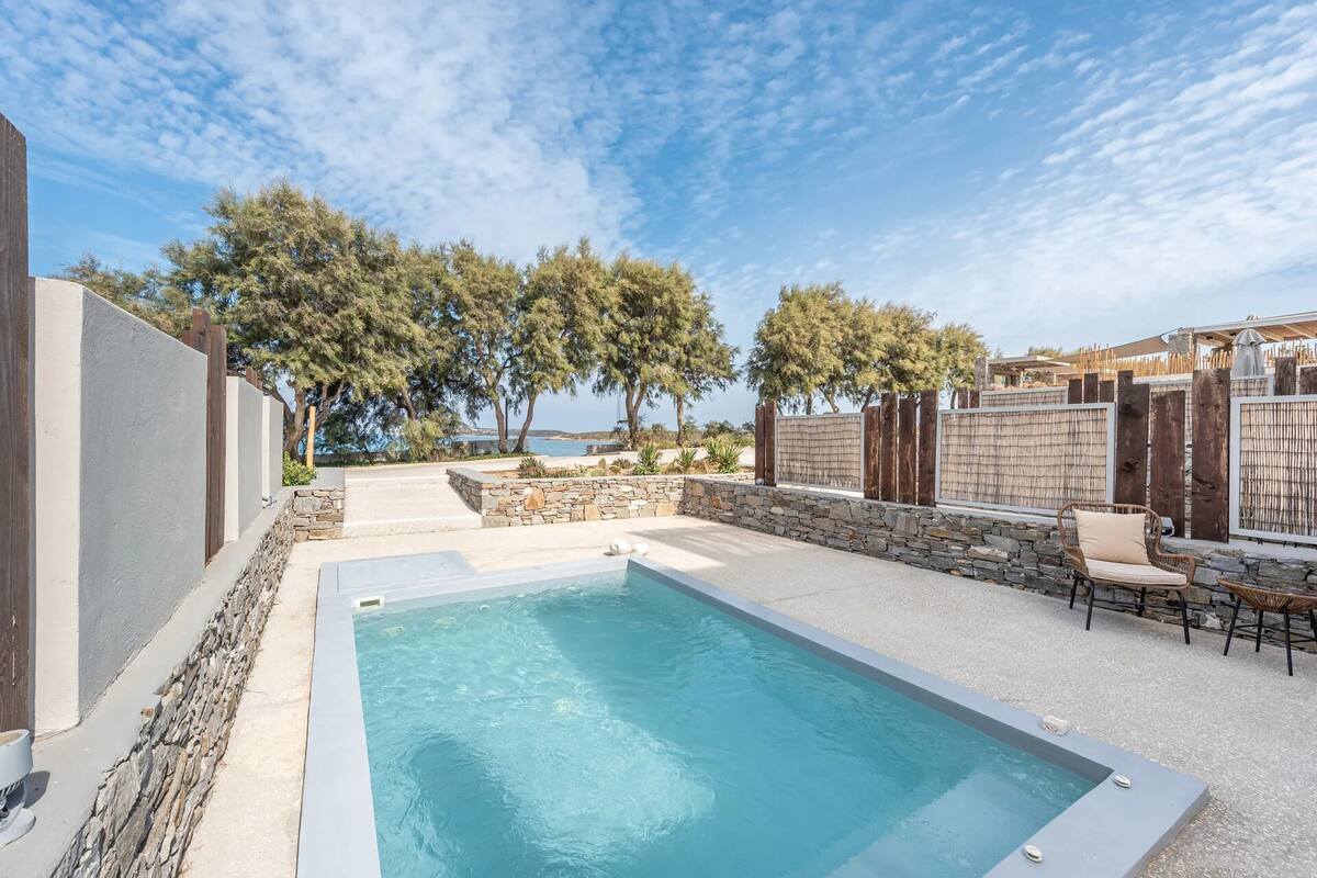 Ein rechteckiger Pool mit Steinrand, umgeben von einer Steinmauer und Holzzaun.