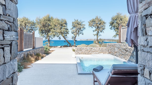 Un arco de piedra que da acceso a una zona de piscina con vistas al mar, rodeada de árboles y muros de piedra.