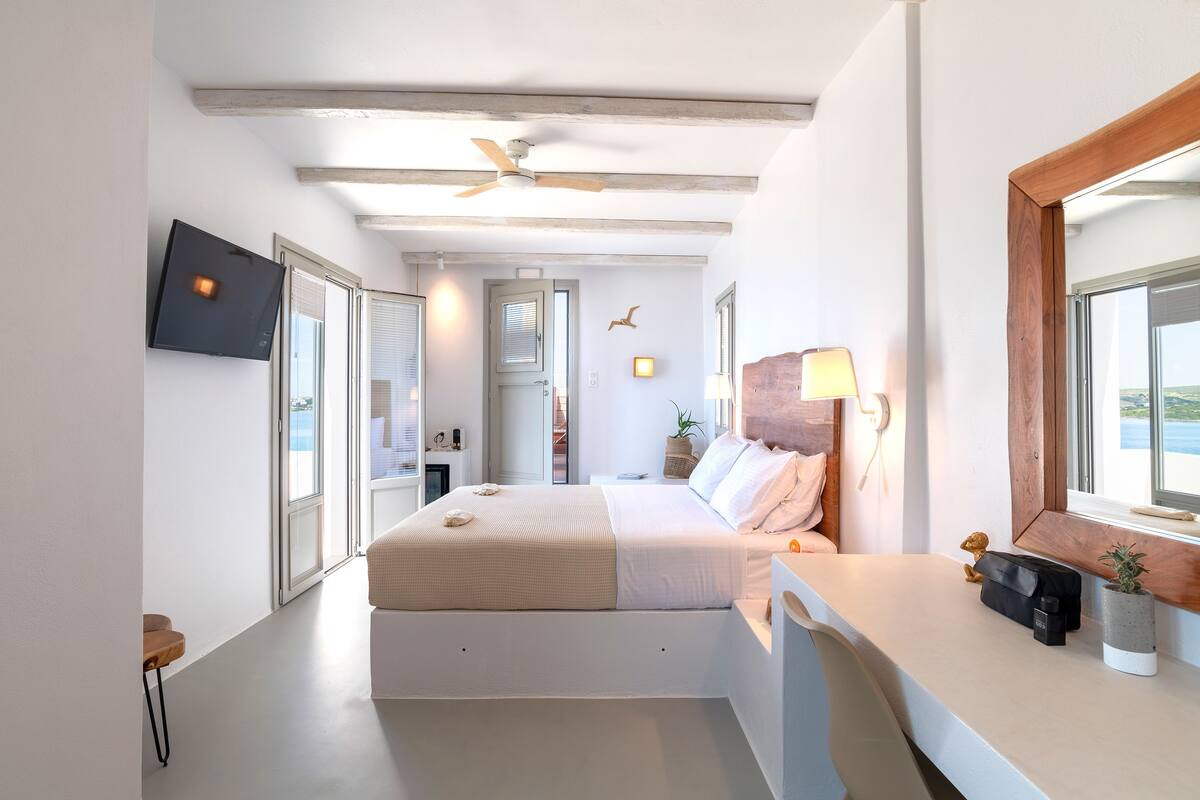 Ein modernes Schlafzimmer mit einem großen Bett, einem Deckenventilator, einem an der Wand befestigten Fernseher und einem Fenster mit Blick.