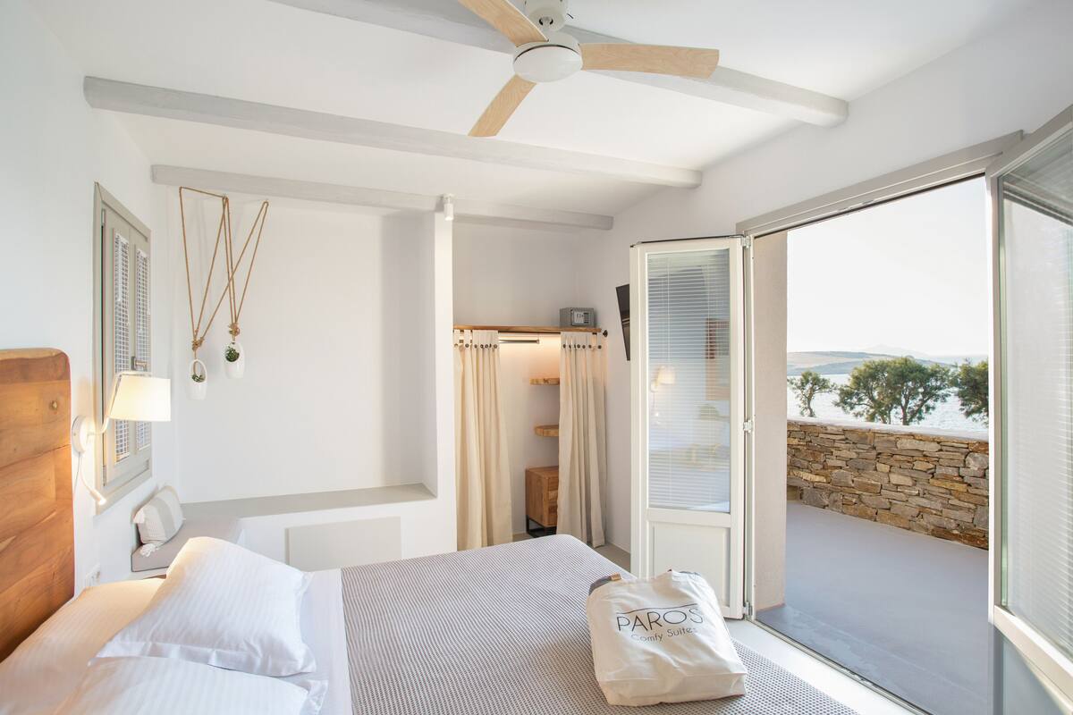 Ein Schlafzimmer mit Bett, Deckenventilator, einem Fenster mit Vorhängen und Blick ins Freie.