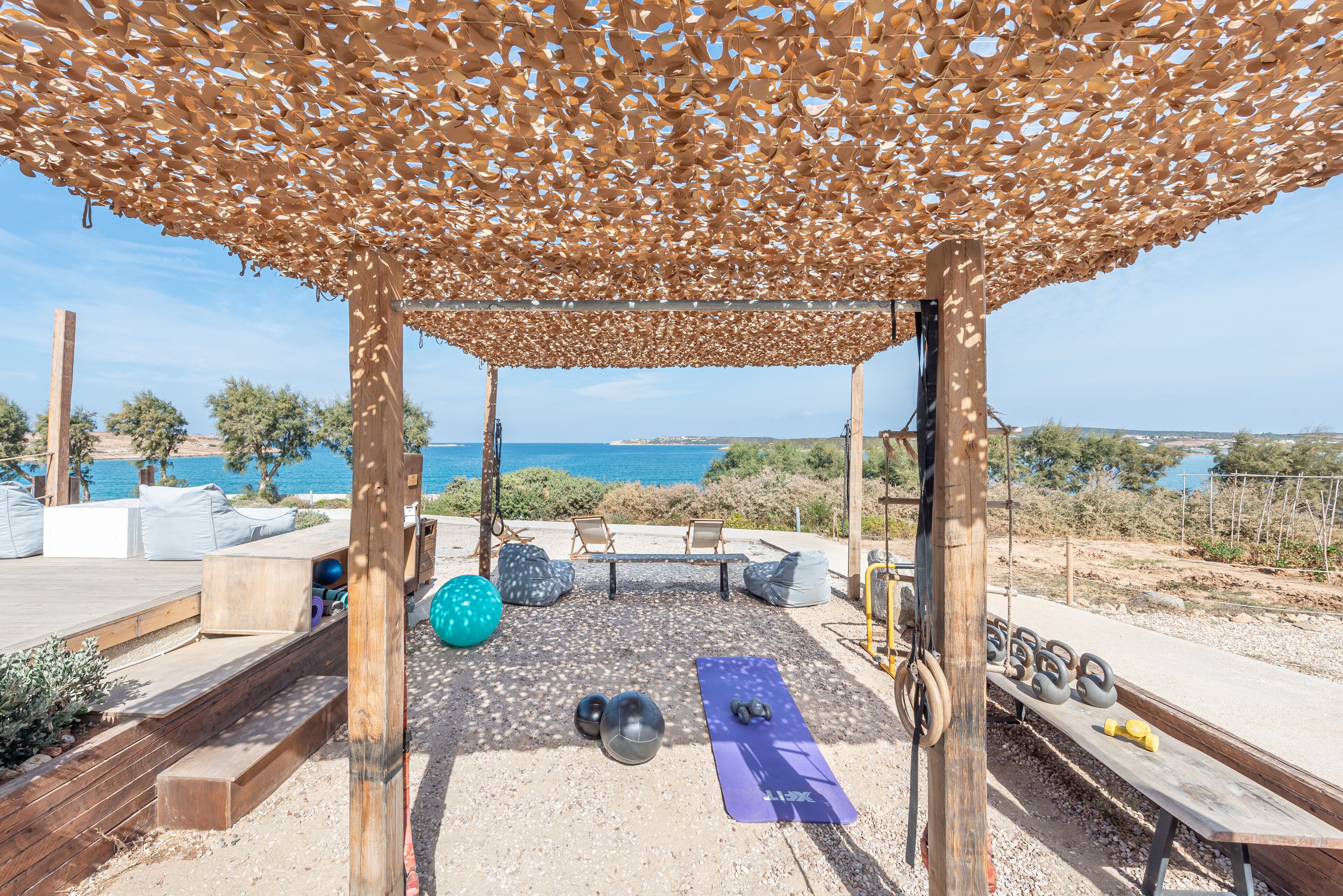 An outdoor gym area with exercise equipment, a yoga mat, and a view of the sea.