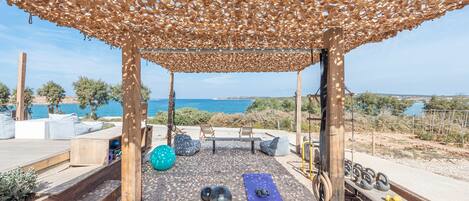 An outdoor gym area with exercise equipment, a yoga mat, and a view of the sea.