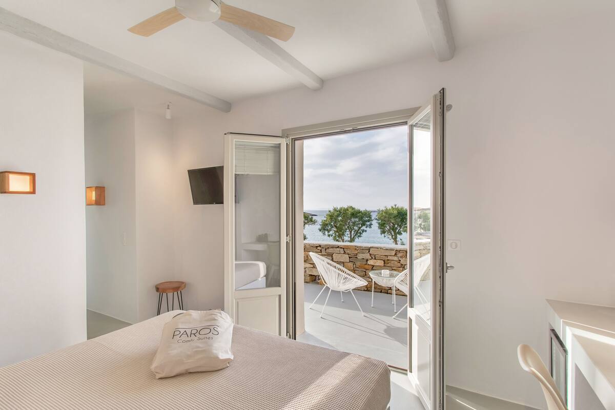 Ein Schlafzimmer mit Bett, Nachttisch, Stuhl und Blick auf einen Balkon mit Steinmauer und Gartenmöbeln.