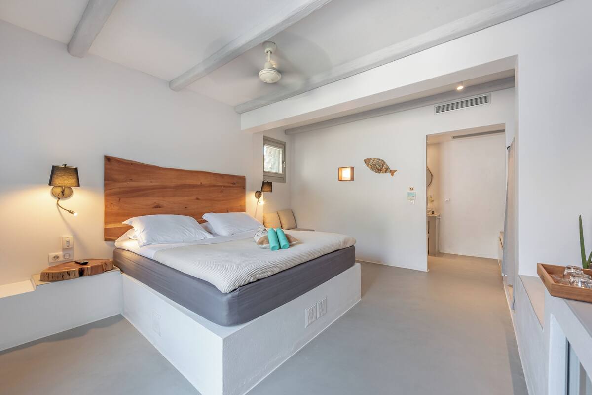 Ein modernes Schlafzimmer mit einem Holzkopfteil, einem großen Bett, Nachttischlampen und einem kleinen Tisch mit einer Pflanze.
