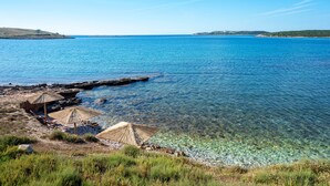 Vista costera con agua cristalina, costa rocosa y sombrillas de paja.