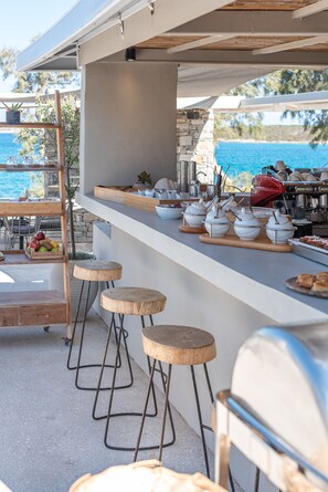 Eine Außenbar mit Meerblick, einem Grill und Hockstühlen.