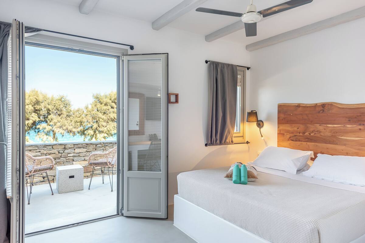 Ein Schlafzimmer mit einem Bett, einem hölzernen Kopfseitenverkleidung, einem Nachttisch, einer Lampe und Blick ins Freie durch eine Schiebetür.