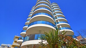 A modern multi-story building with a curved facade, large windows, and balconies. - Residence Sky (Lignano Sabbiadoro)