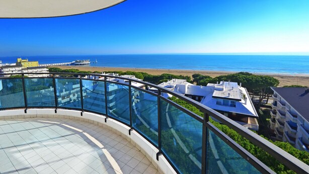 A high-rise building with a glass balustrade overlooking a beach. - Residence Sky (Lignano Sabbiadoro)