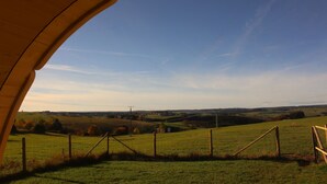 A view through a wooden archway overlooking a green field with a fence and distant hills.