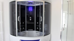 A modern, enclosed room with a glass door, a control panel, and a blue light fixture.