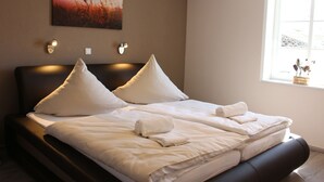 A neatly made double bed with white linens and pillows, a headboard, and a painting of a sunset on the wall.