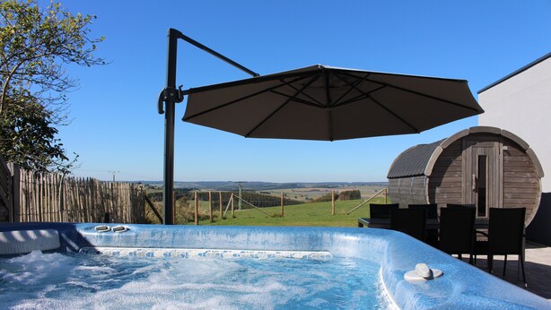 A hot tub with a view of the countryside, a wooden structure, and outdoor furniture.
