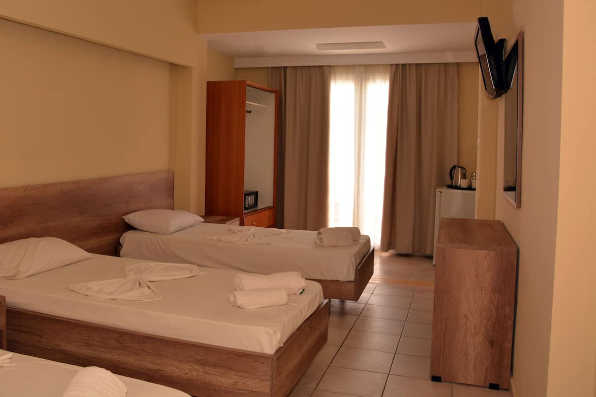 A hotel room with two beds, a wooden wardrobe, a desk with a kettle, and a mirror on the wall.