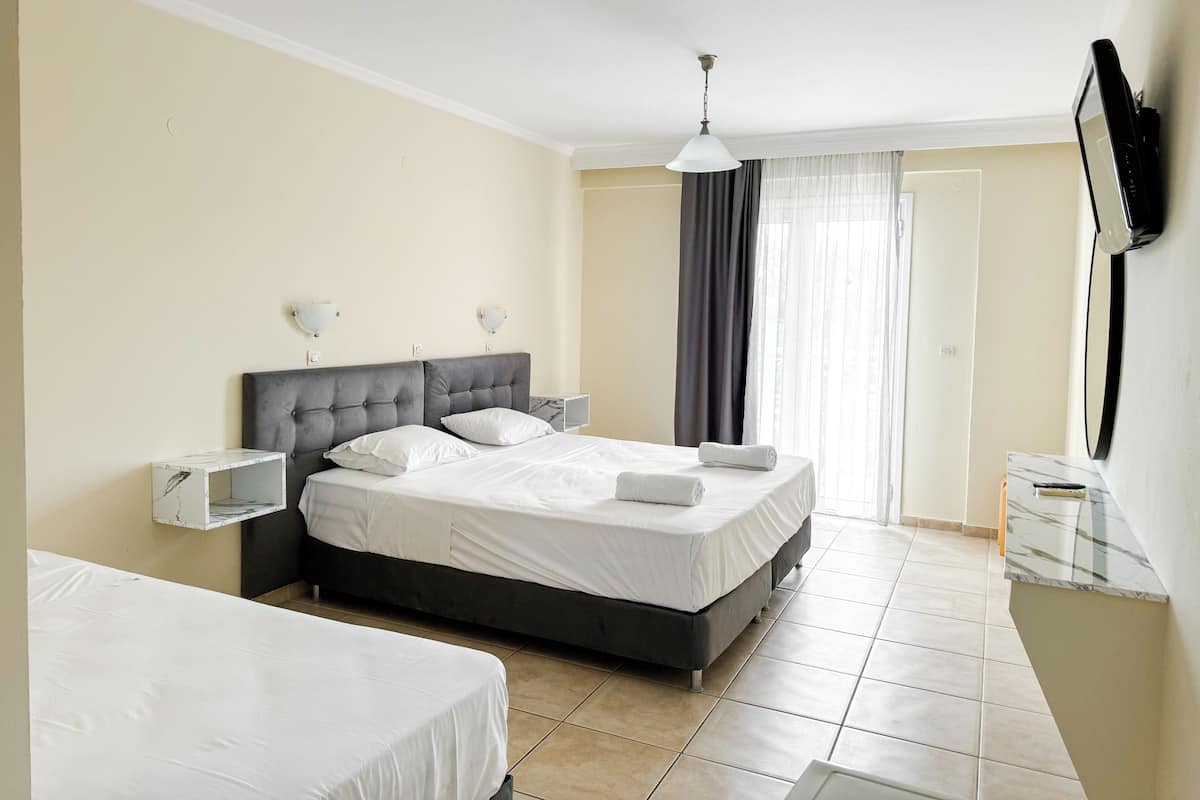 A hotel room with a large bed, bedside tables, a TV, and a window with curtains.