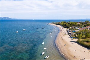 Una playa costera con barcos fondeados cerca de la orilla, arena y una hilera de edificios con techos rojos.