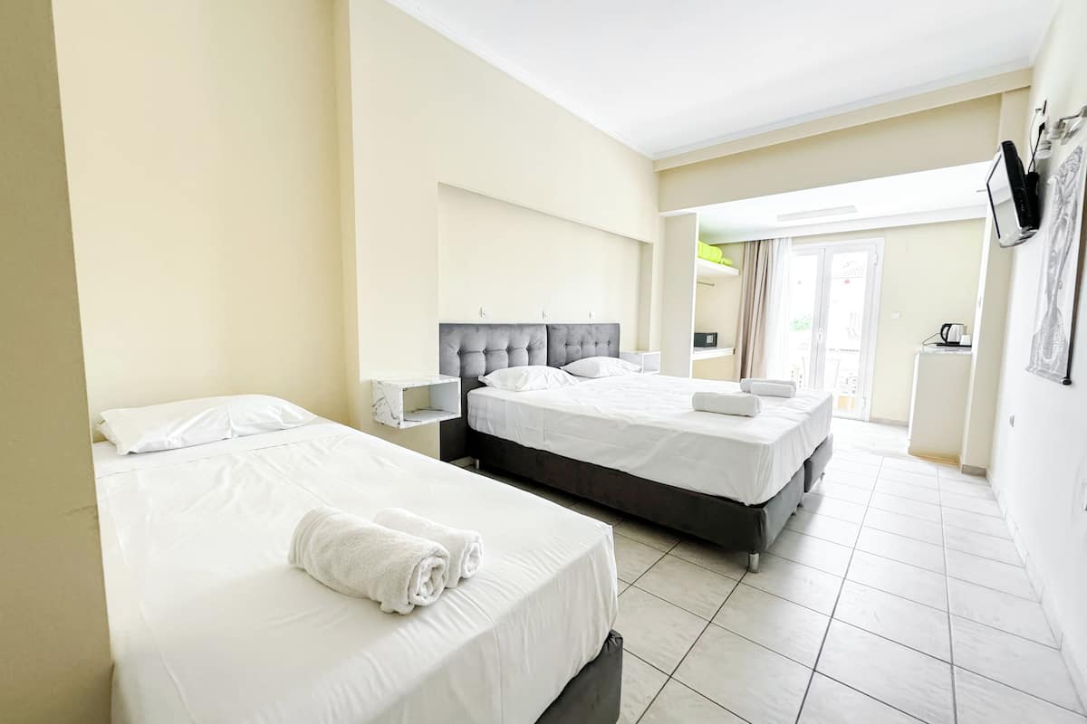 A hotel room with two beds, a small bedside table, a headboard, and a view of the hallway.