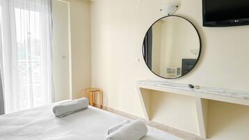 A hotel room with a bed, a round mirror, a TV, and a small stool.